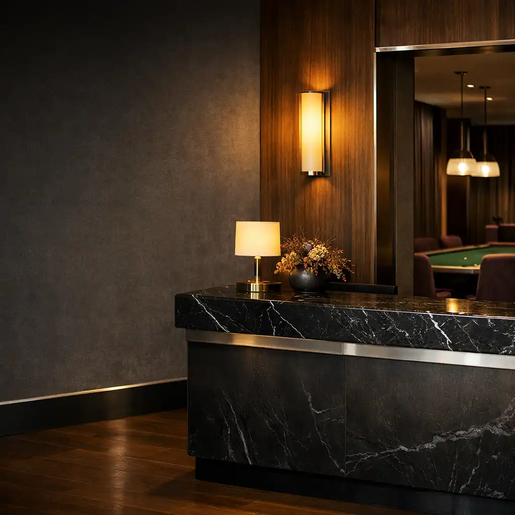 Warmly lit dark lounge arrival area with a marble host surface and green felt poker table deeper in the room